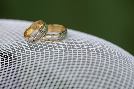 Golden wedding rings on the white mesh with green background.の写真素材