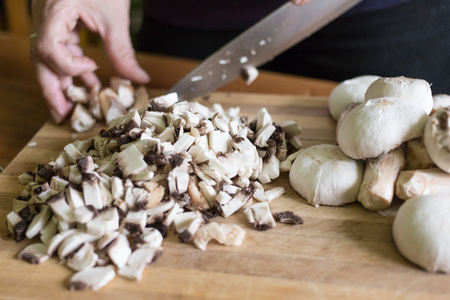 A woman cuts mushrooms with a knife on a wooden cutting board.の写真素材