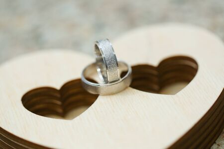 Two wedding rings on wooden case in heart shape. Close up macro shot of silver rings
