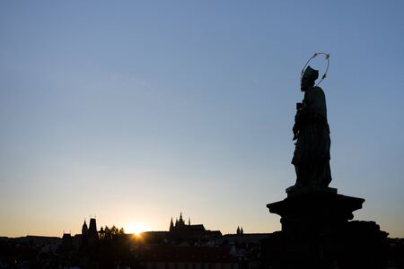 Silhouette of St. John of Nepomuk's Statue on Charles Bridge in Prague with St. Vitus Cathedral in background at sunset.の写真素材