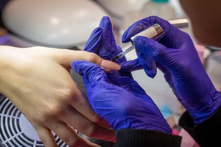 Manicurist with blue gloves polish nails on women's hand in nail salonの写真素材