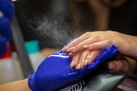 Manicurist with blue gloves spraying nails on women's hand in nail salon.の写真素材