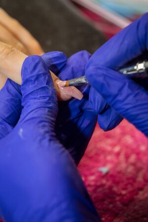 Manicurist with blue gloves polish nails on women's hand in nail salonの写真素材