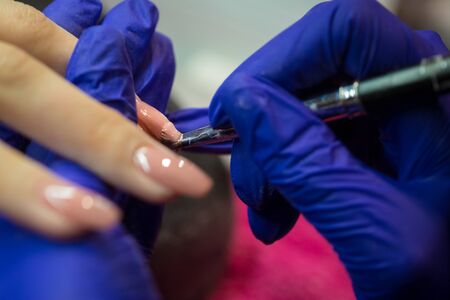Manicurist with blue gloves polish nails on women's hand in nail salonの写真素材