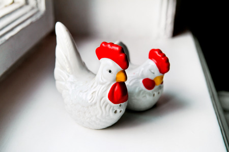 Two ceramic figurines of chickens by the windowの写真素材