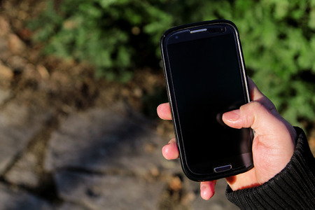 Human hands holding a smartphone and playing game or online social network outdoors. Business man...