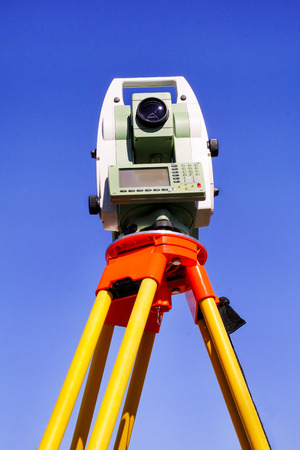 Total station with blue sky in the background. Survey Instrument geodetic device, total station set in the field. Total station surveying and measuring engineering equipment at work in garden.の写真素材