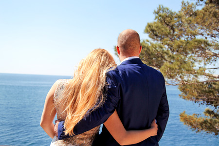 Wedding. Happy couple day wedding. Beautiful bride and groom at the beach. Cheerful married couple standing on the shore and watch the sea. Wedding couple staying over beautiful landscape.の写真素材