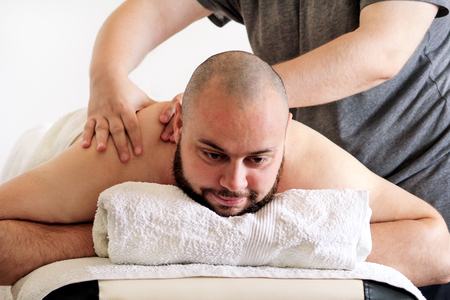 Massage studio. Sports massage. Massage therapist massaging shoulders of a male athlete, working with neck muscles. Body care. Man having massage in the spa body massage salon. Massage table.の写真素材