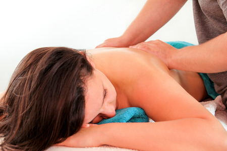 Massage relax studio. Woman laying on massage table and having a massage back. Beautiful girl is enjoys, on front of her body while a massage therapist is massaging her shoulders. Body care.の写真素材