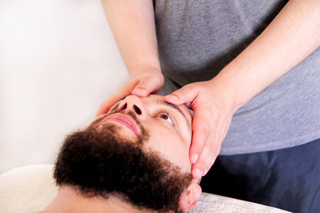 Man having treatment for his face at massage table, medicine concept. Masseur massaging mans face. Handsome man relaxing receiving facial massage at spa center relaxation therapy resort recreation.の写真素材