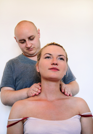 Massage professional studio. Spa treatment. Man relaxing getting neck and shoulder massage. Masseuse human hands massaging for neck. Smiling woman sitting and having neck massage in medical office.の写真素材