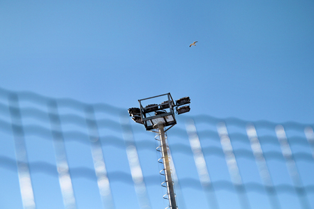 Stadium floodlight tower with reflectors with blue sky. Lighting pole tower at the sports stadium and ground. Big lamp and light stadium poles or sports lighting. Flood light pole in the spotlight.の写真素材
