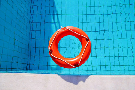 Red lifebuoy pool ring float, ring floating in refreshing blue swimming pool. Red float floating in the pool with blue water. Inflatable red swim ring floating on a pure water with sunny reflections.の写真素材