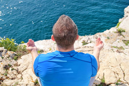 A fit man in the Lotus position on a seashore. Young fitness man doing yoga outdoors. Practicing yoga, meditation, pilates and stretching. Handsome sportsman in yoga class in lotus position.の写真素材