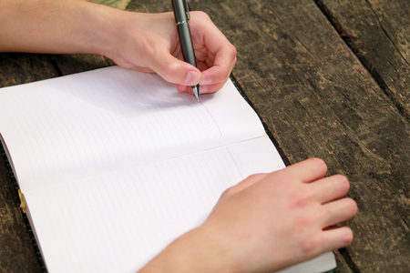Young handsome guy sitting at wooden table, writing a book, doing homework, taking notes, learning,...