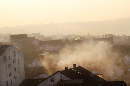 Smoking chimneys at roofs of houses emits smoke, smog at sunrise, pollutants enter atmosphere.の写真素材