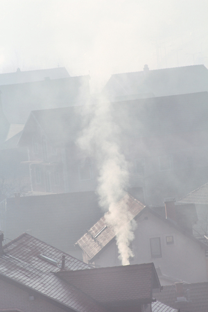 Smoking chimneys at roofs of houses emits smoke, smog at sunrise, pollutants enter atmosphere.の写真素材