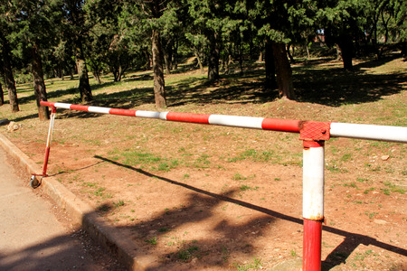 Red and white warning sign barrier on green grass in nature background. Transport, traffic regulation. Old fence made and white and red street parking barrier ramp, control point, forbidden territory.の写真素材