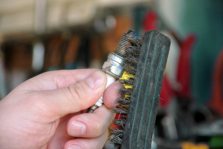 Cleaning a car engine spark plug with wire brush in car garage.