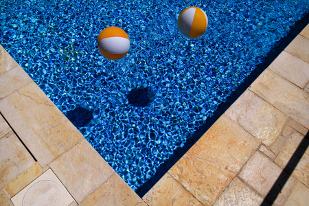 Two rubber air yellow white inflatable balls and toy for swimming pool in transparent blue water.
