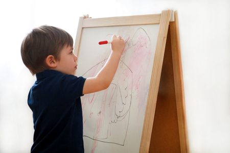 Child is drawing and painting with felt pen on paper of wooden drawing board artist easel for kids and children at home.の写真素材