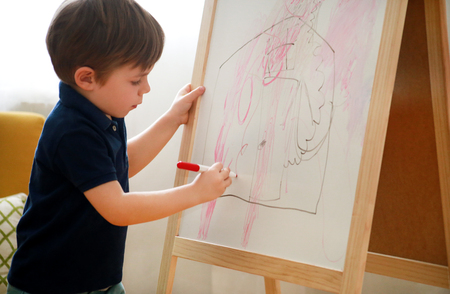 Child is drawing and painting with felt pen on paper of wooden drawing board artist easel for kids and children at home.の写真素材