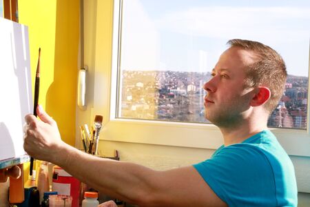 Portrait of handsome artist measuring proportions with paintbrush. Male artist painter working in...