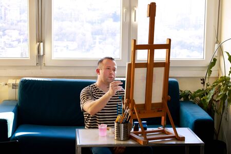 Male artist painter working in workshop with canvas on wood drawing board easel in art paint studio....