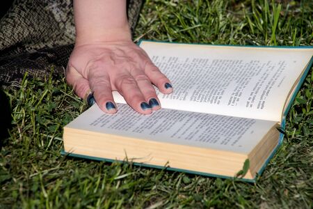 Nice fashion woman lies on green grass and reading an interesting book in city park at summer day. Handsome student woman is sitting and reads book, study and enjoys in beautiful natural environment.の写真素材