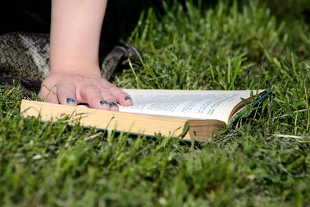 Nice fashion woman lies on green grass and reading an interesting book in city park at summer day. Handsome student woman is sitting and reads book, study and enjoys in beautiful natural environment.の写真素材