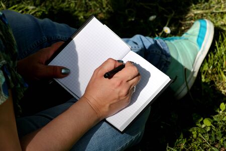 Woman and student sitting on grass, takes notes in notebook