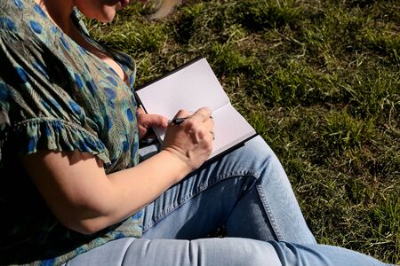 Woman and student sitting on grass, takes notes in notebook, learning and writes thoughts, writes...