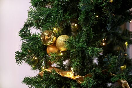 Traditional decorated baubles hangs on green twigs tree of pine. Bright gold balls on Christmas tree of fir or spruce with string rice lights bulbs. Ornaments to christmas celebration, holiday scene.の写真素材