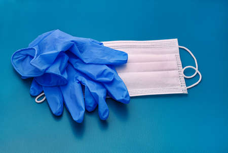 Pair of medical blue latex protective gloves and white mask on blue background. Protection equipment...