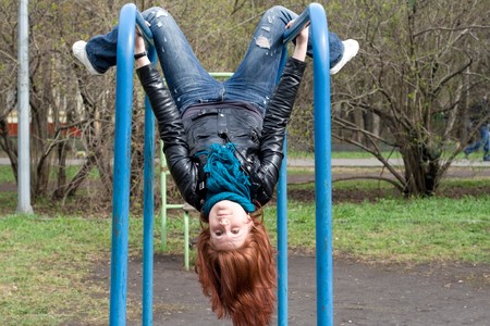 Sportive girl hanging on horizontal bar outdoor