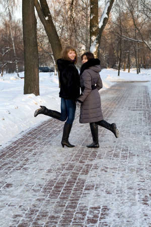 Two female friends walking in park in winterの写真素材