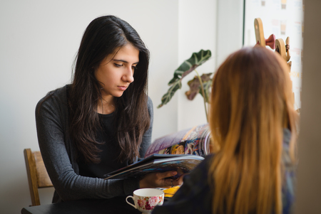 Girls in a cafe talking. Two girls drink coffee in a cafe and talk. A girl in a cafe reading a magazineの写真素材