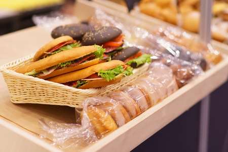 A black burger with tomato and salad and sausage on a display case lieの写真素材