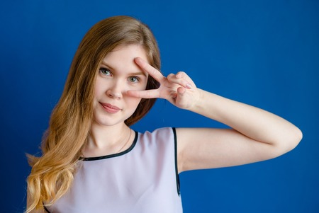 Blonde girl on blue background shows sign peaceの写真素材