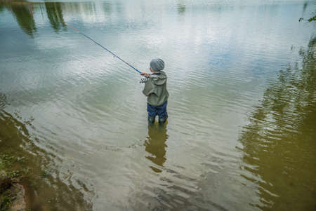 boy catching fish standing in water in big boots