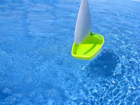 yellow toy boat sails across a pool of blue waterの写真素材