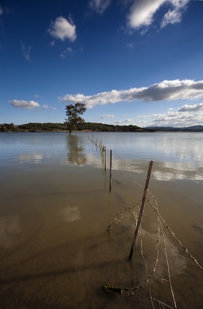 Lake with the sky reflected in water and a fenceの写真素材