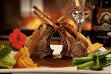 close up on roast lamb cutlets with vegetables and gravy on a white plate in a restaurant settingの写真素材