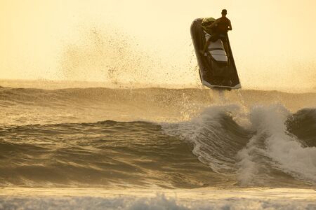 Silhouette of man riding a water scooter and jumping over a wave on sunrise