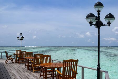 Maldives wooden cafe tables and chairs on a tropical sea, with a beautiful view of turquoise shallow waterの写真素材