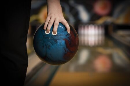 ten pin bowling ball being held in hand by bowler close up, with bowling lane and ten pins blurred in the background, copy spaceの写真素材