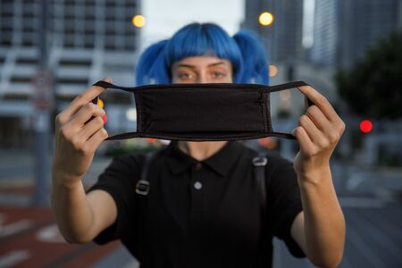 young female using medical mask in city, stylish trendy girl with blue hair wearing fashionable...