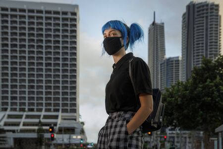 young female wearing medical mask in modern city street, stylish trendy girl with blue hair wearing fashionable protective medical mask amid coronavirus fears, covid19 pandemic, new fashion conceptの写真素材
