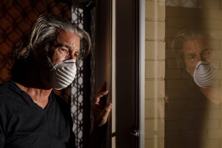 coronavirus crying male medical mask quarantine, self isolation concept, depressed distraught mans reflection in window with tears wearing protective mask. covid-19 virus pandemic, healthcare crisisの写真素材